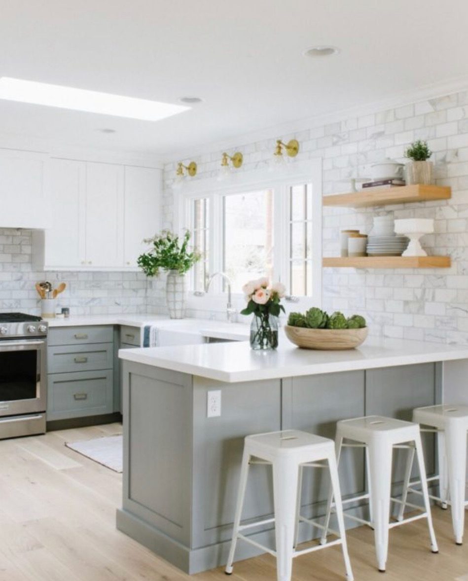 White kitchen with a grey island, floating wood shelves, and pendant lighting